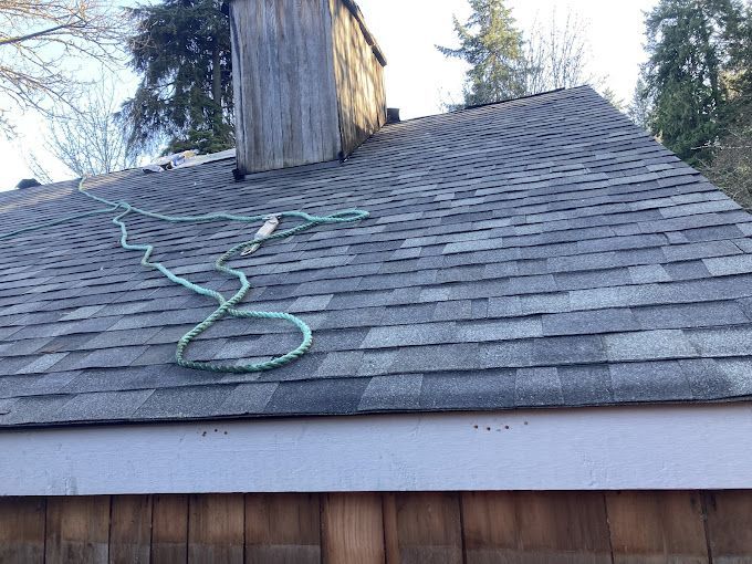 A green hose is hanging from the roof of a house.