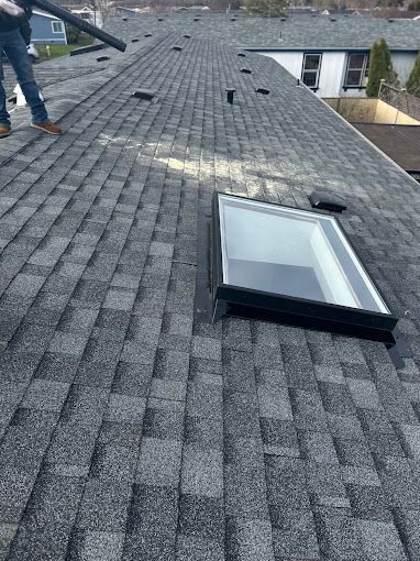 A man is standing on top of a roof with a skylight.
