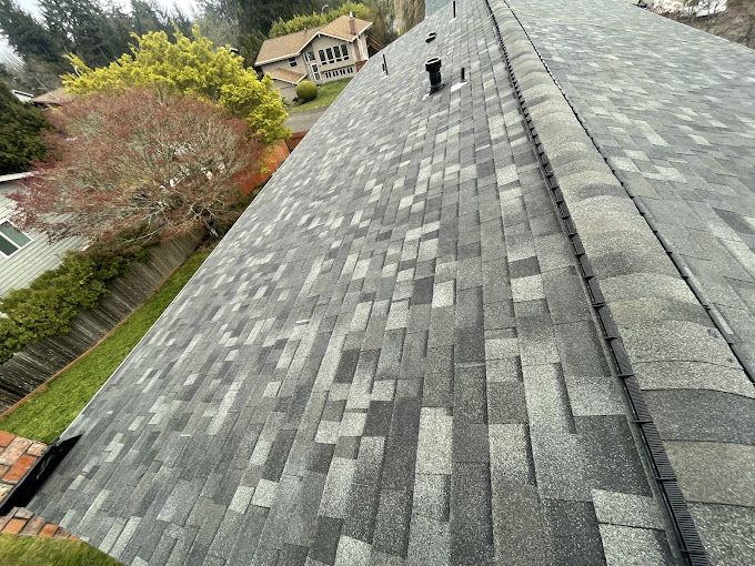 A roof with a lot of shingles on it and a house in the background.