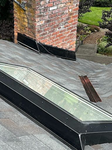 A skylight is sitting on top of a roof next to a chimney.