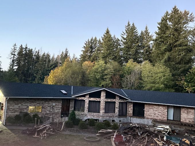 A large brick house with a black roof is surrounded by trees.