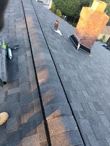A person is working on a roof with shingles and a chimney.