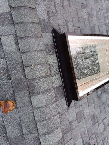 A person is standing on a roof next to a skylight.