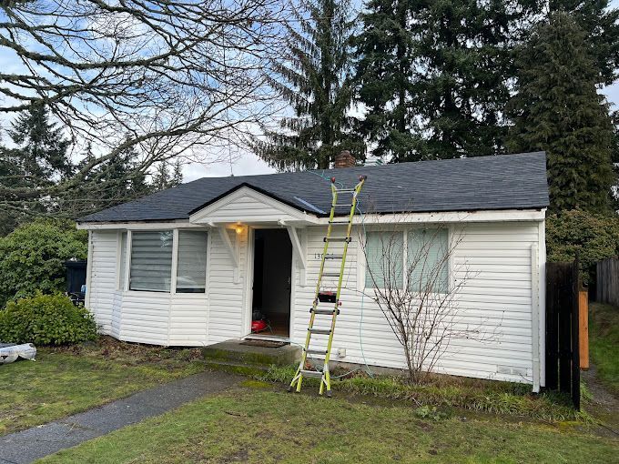 A white house with a black roof and a ladder in front of it.
