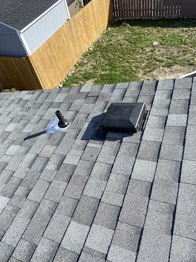A roof with a vent on it and a wooden fence in the background.