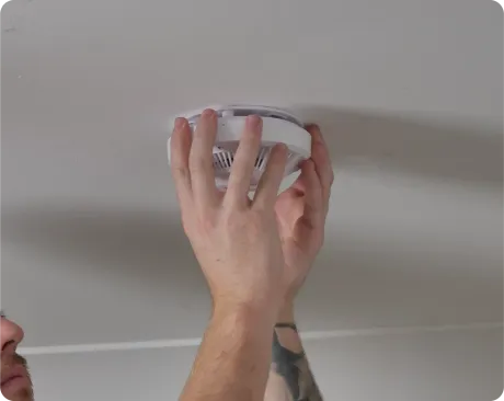 Person installing a white smoke detector on a white ceiling.