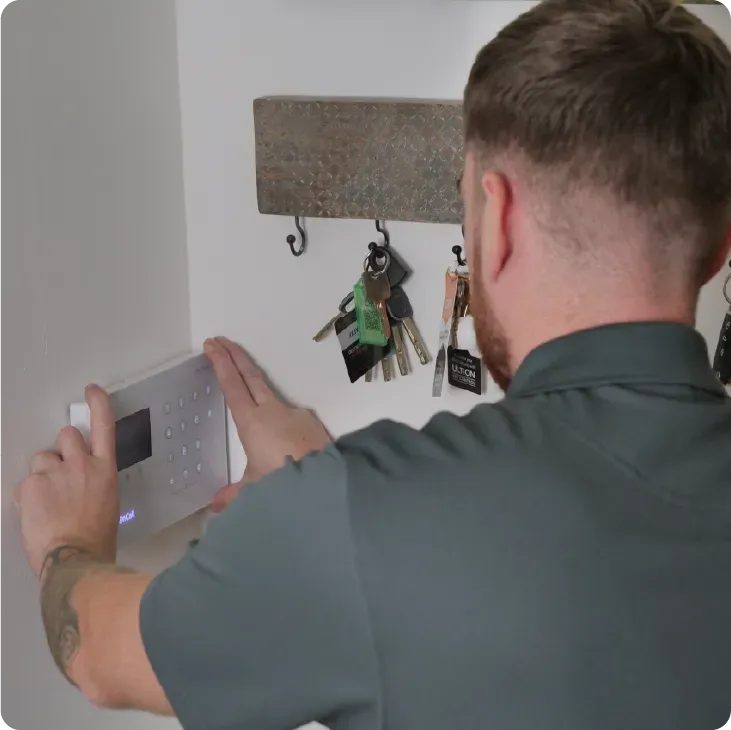 Person installing a security panel on a white wall, near a key holder.
