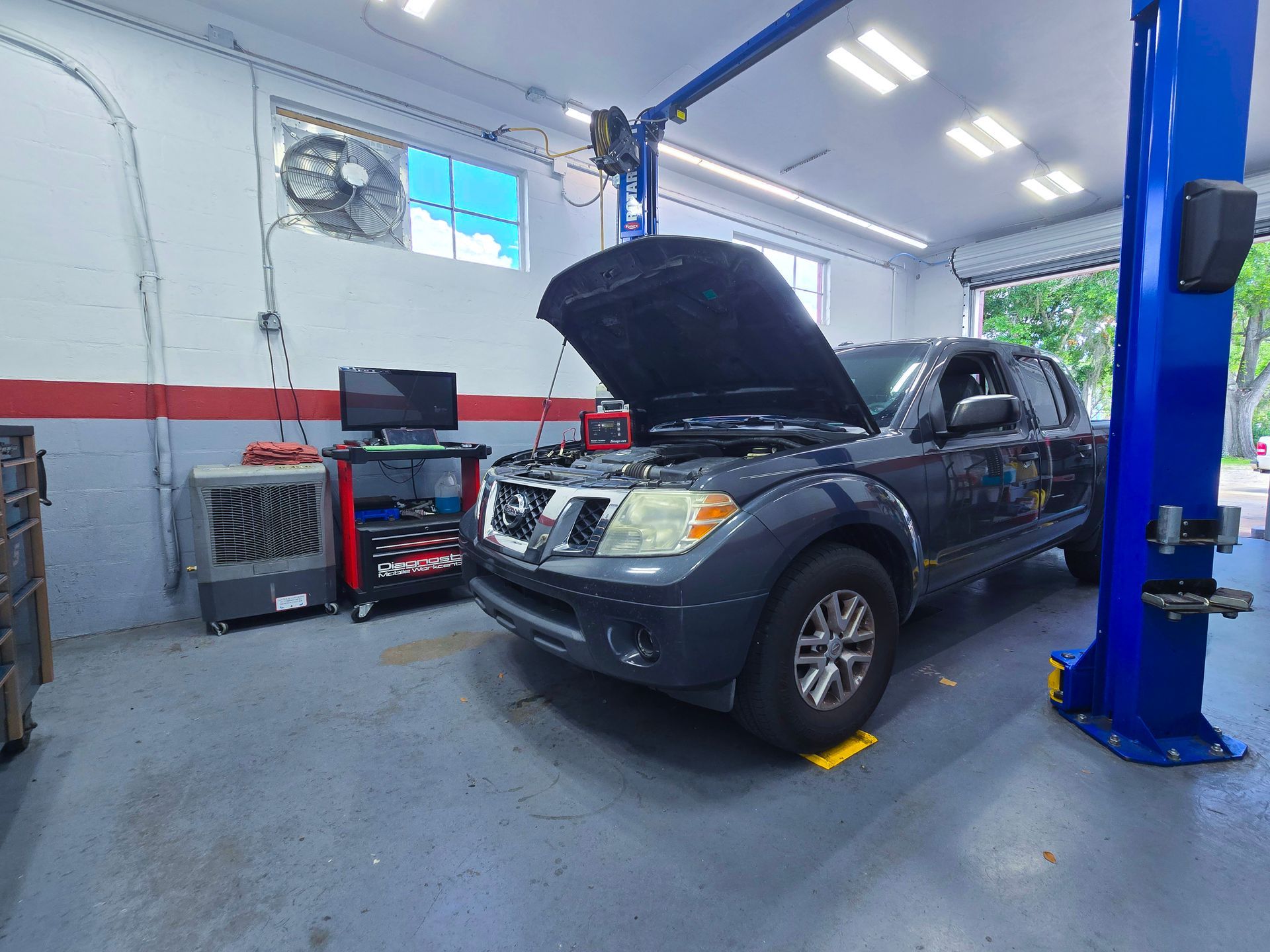Nissan truck in a mechanic's shop with hood open. Blue lift posts and diagnostic equipment. | Johnny's Automotive