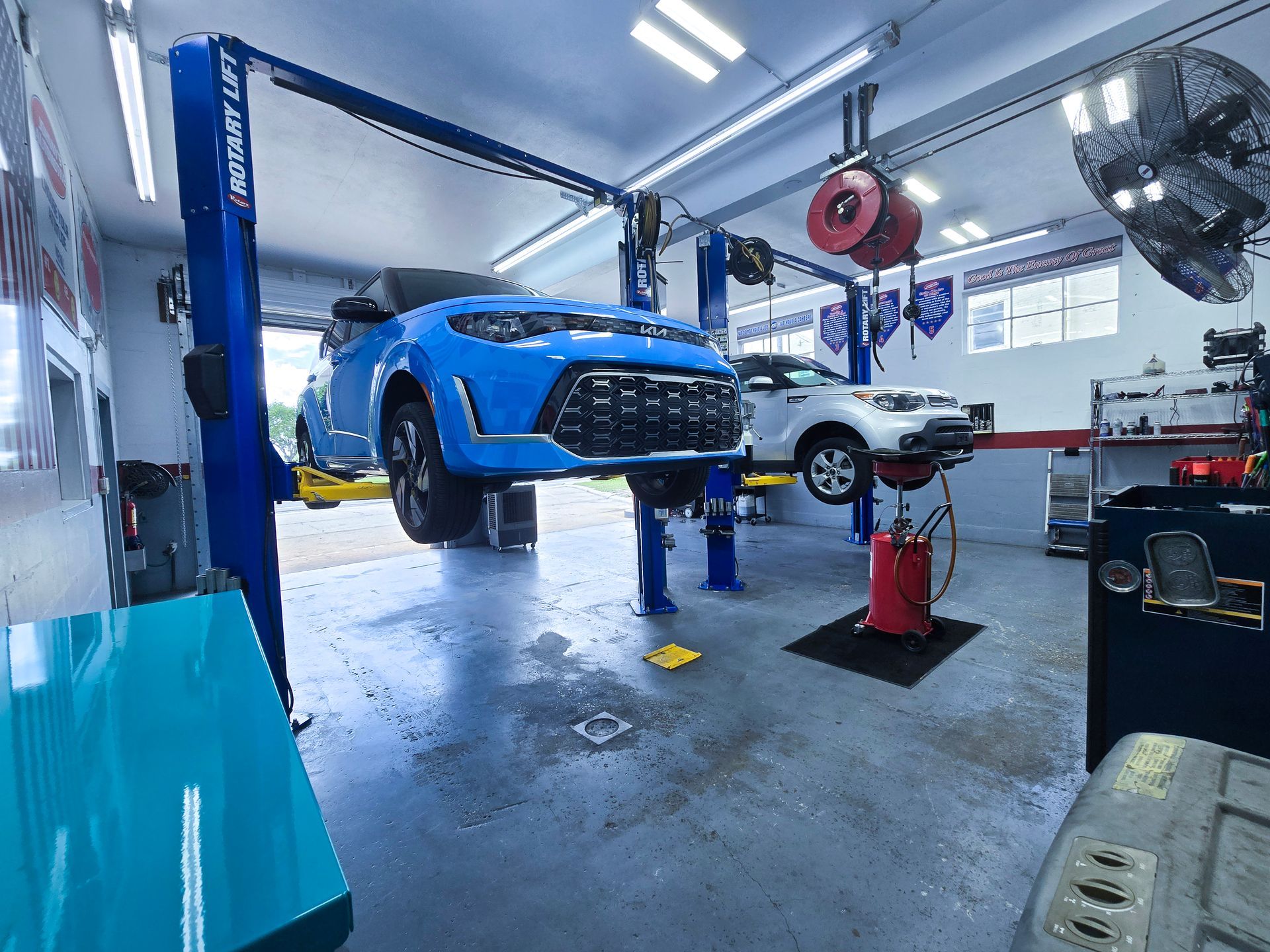 Two cars lifted on hoists in a brightly lit auto repair shop. One blue, one white. | Johnny's Automotive