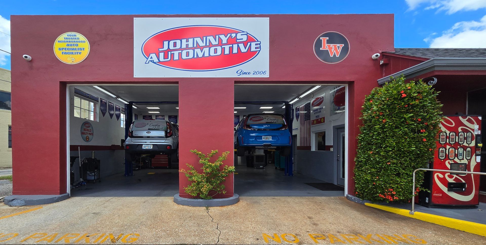 Johnny's Automotive garage exterior with cars on lifts. Red facade, blue sky. Vintage signs. | Johnny's Automotive