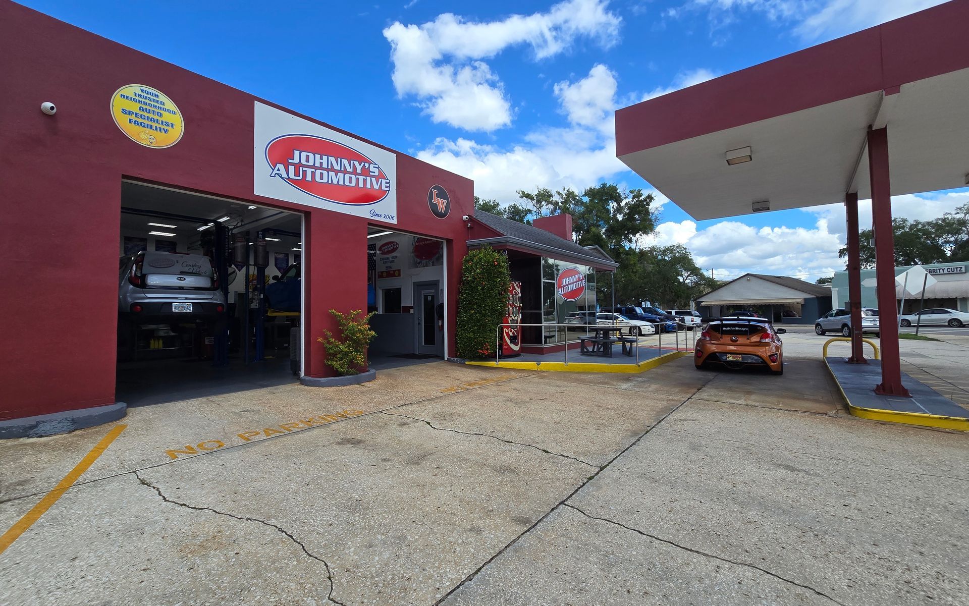 Exterior view of John's Automotive, a red building with a car on a lift, a gas pump, and cars parked outside. | Johnny's Automotive