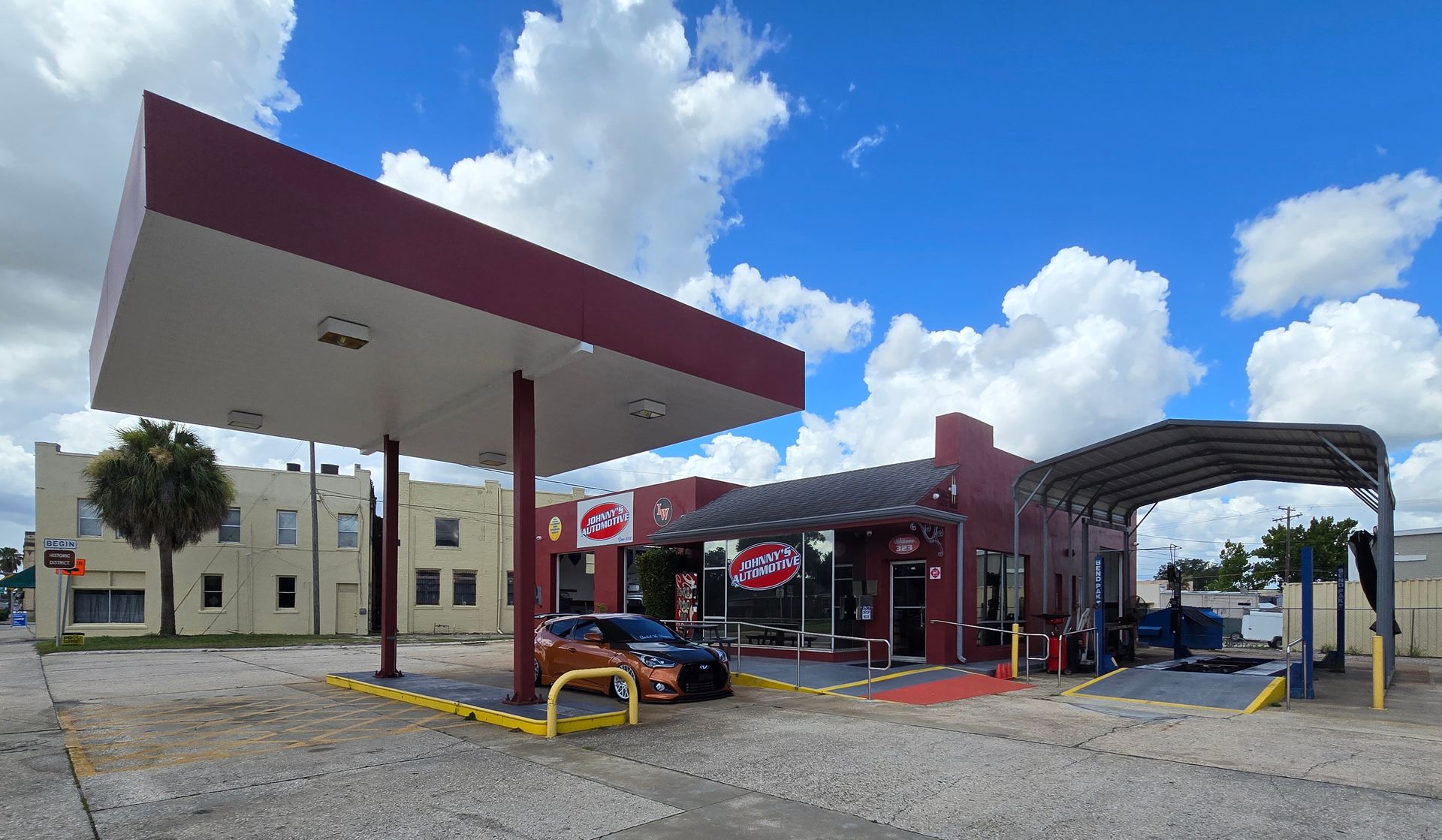 Auto repair shop with maroon accents, a canopy, and a car on a sunny day. | Johnny's Automotive