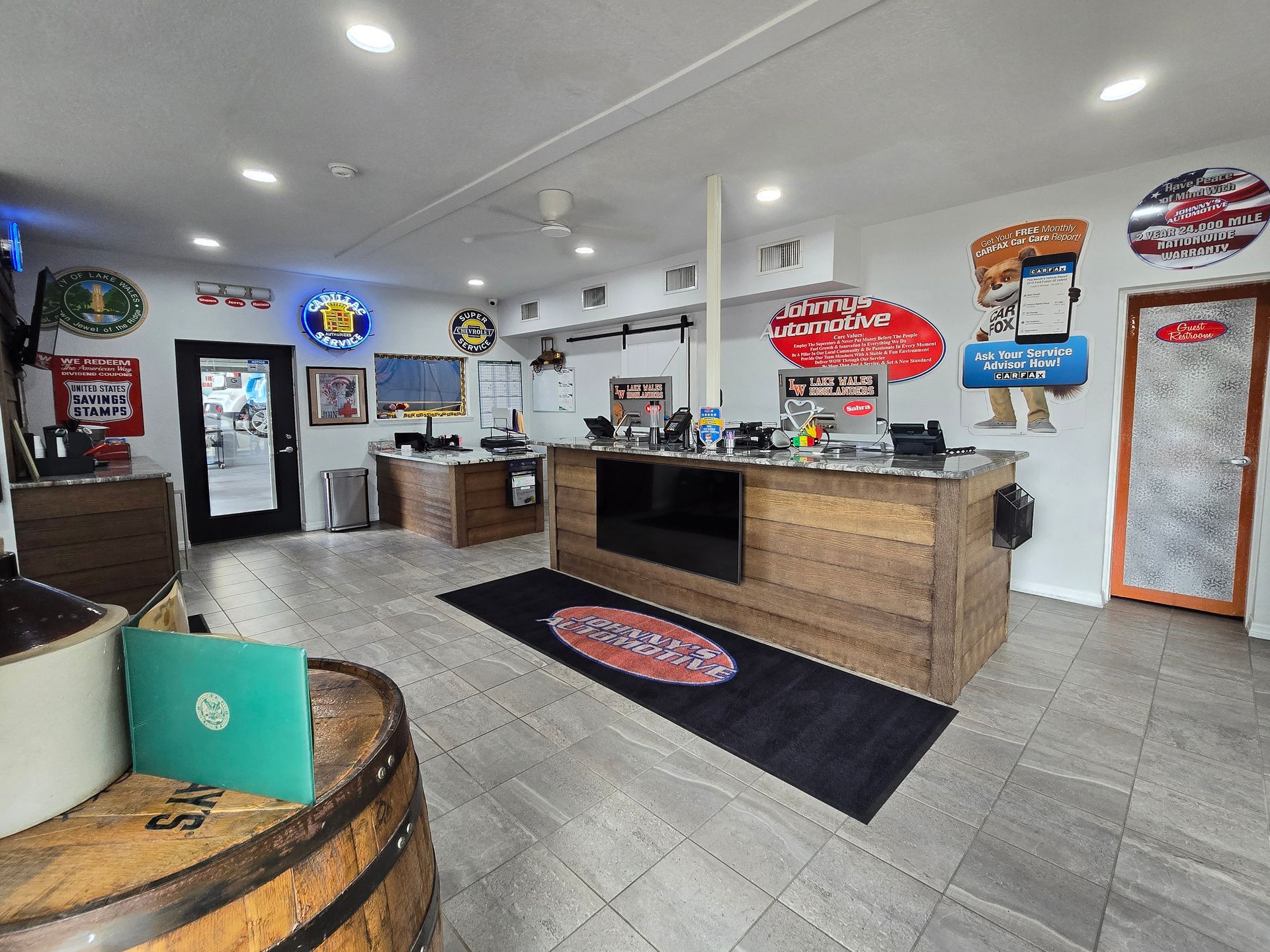 Interior of a business: a bar-like counter, decorative signs, and a barrel with items on top. | Johnny's Automotive