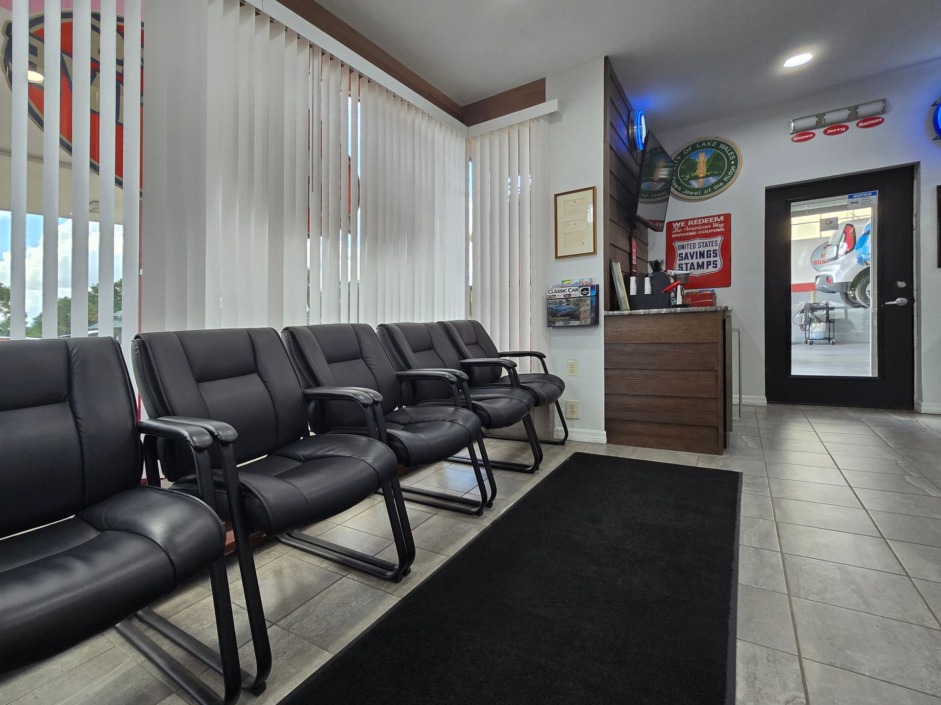 Waiting room with black chairs, window blinds, and a view into a garage. | Johnny's Automotive