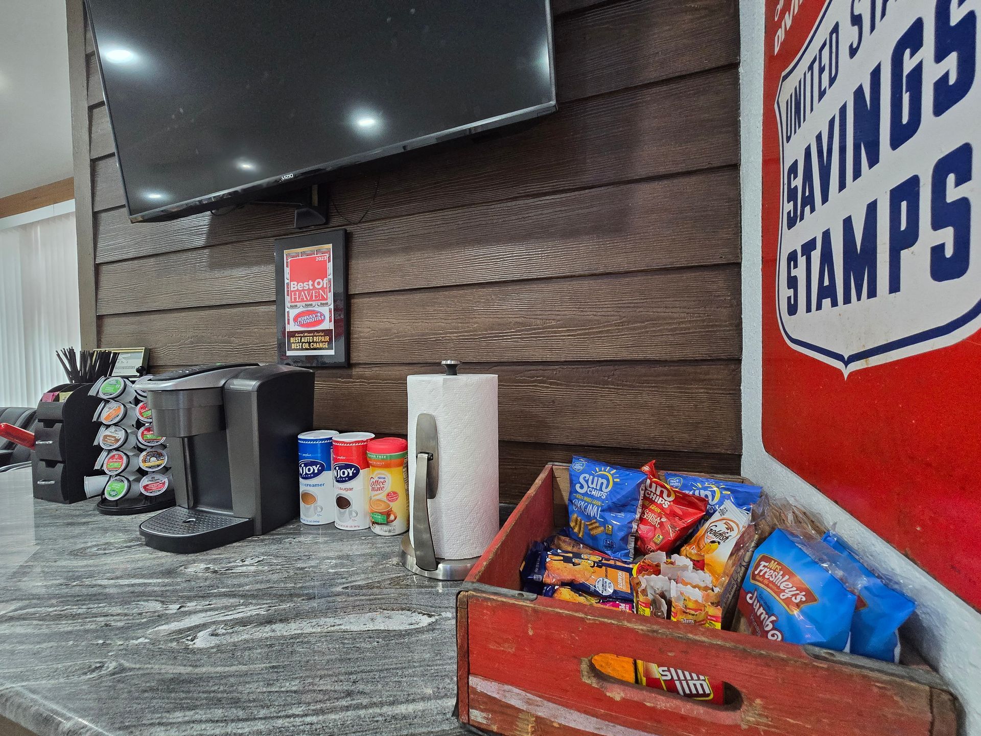 Coffee station with snacks, coffee maker, and a vintage US Savings Stamps sign. | Johnny's Automotive