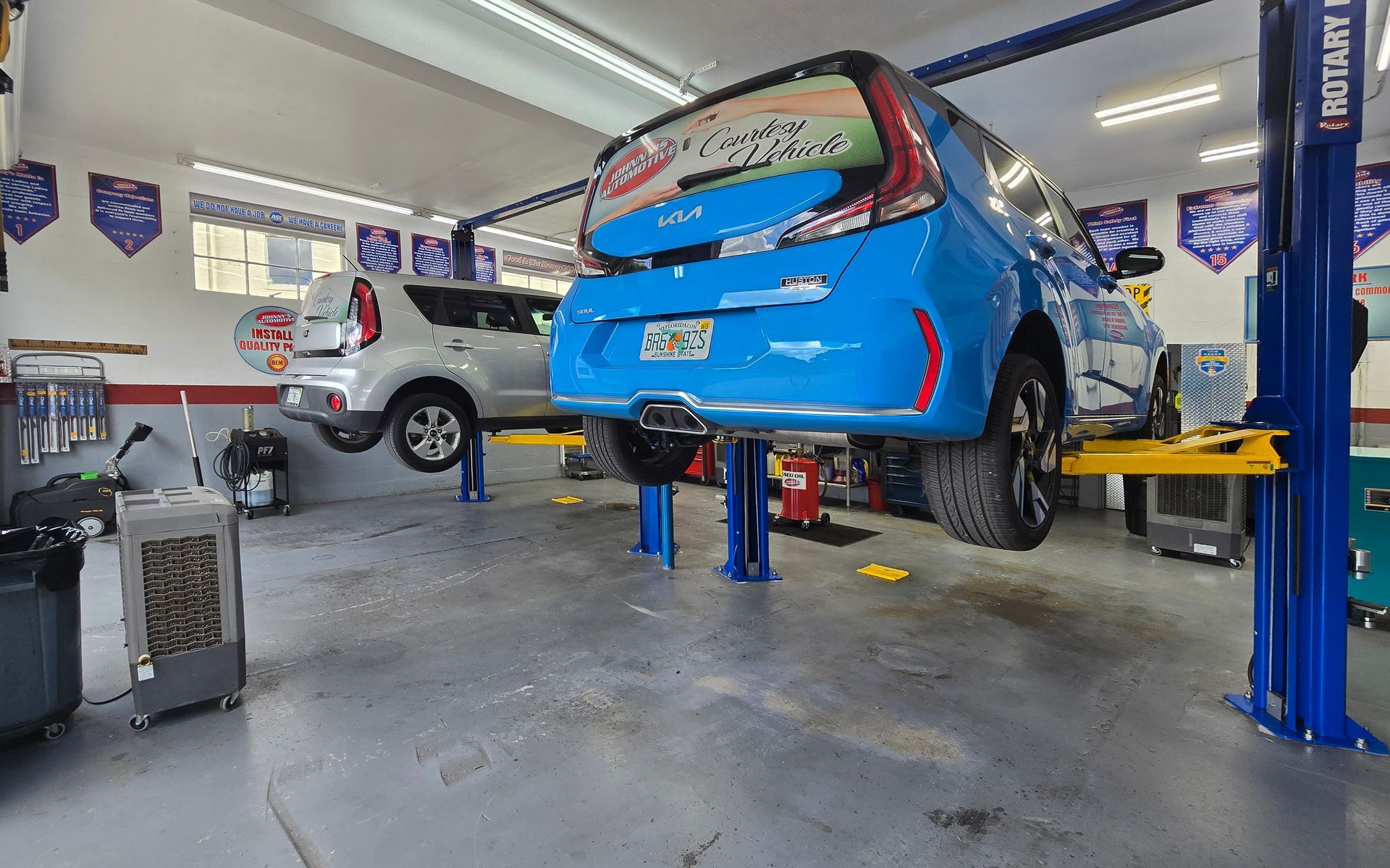 Two cars on lifts in a repair shop. One is blue, one is silver, both are elevated for service. | Johnny's Automotive