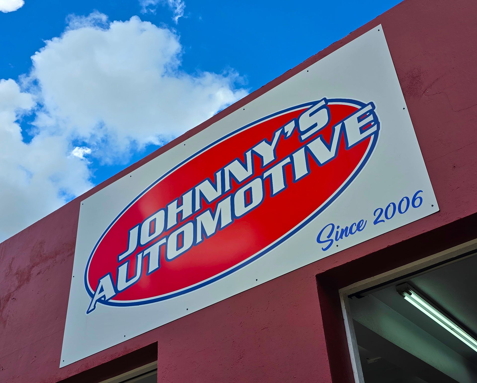 Johnny's Automotive sign on a red building, white background with red and blue text.
