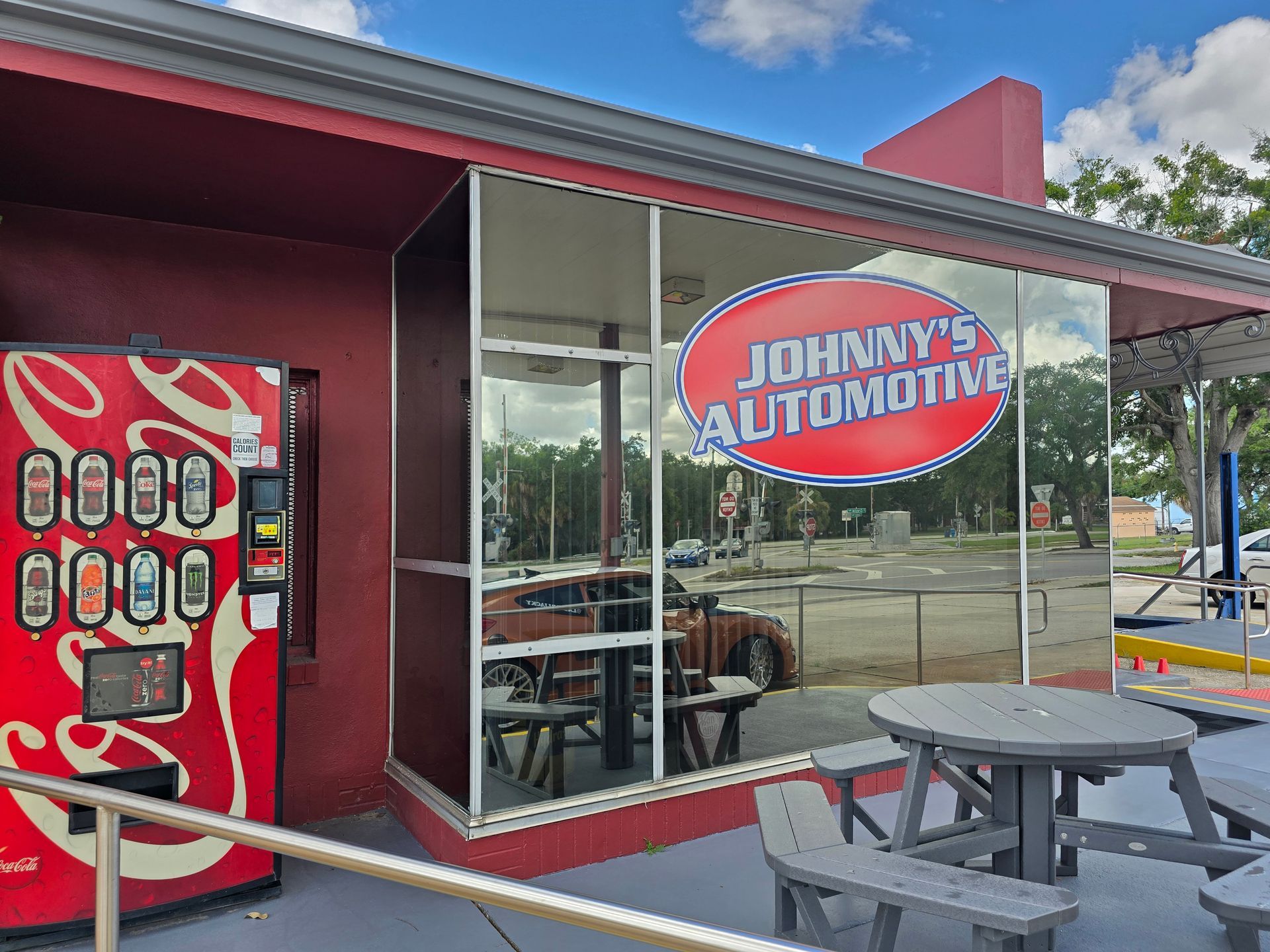 Johnny's Automotive shop with a red exterior, a Coca-Cola vending machine, and a round picnic table. | Johnny's Automotive