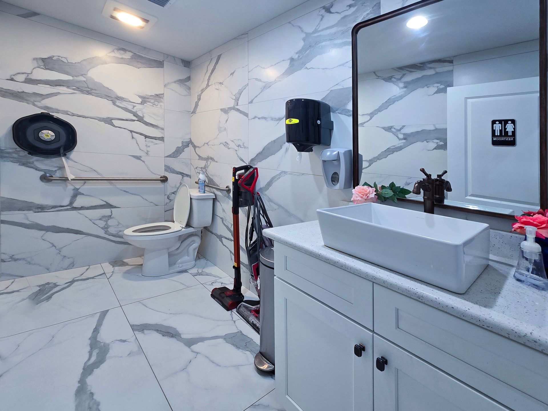 Accessible bathroom with marble walls, a toilet, a sink, and a hand sanitizer dispenser. | Johnny's Automotive