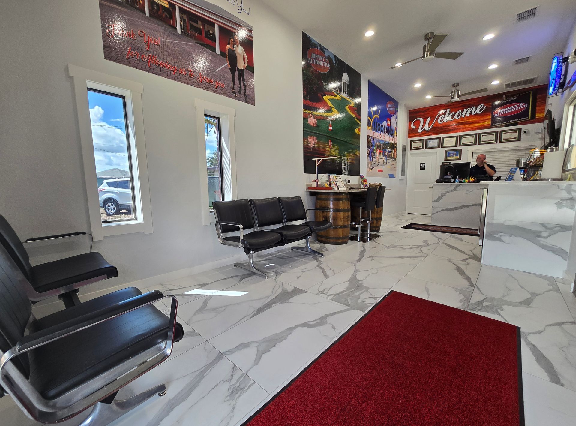 Interior of a modern waiting area; black chairs, red rug, marble floors, with large art pieces and a desk. | Johnny's Automotive