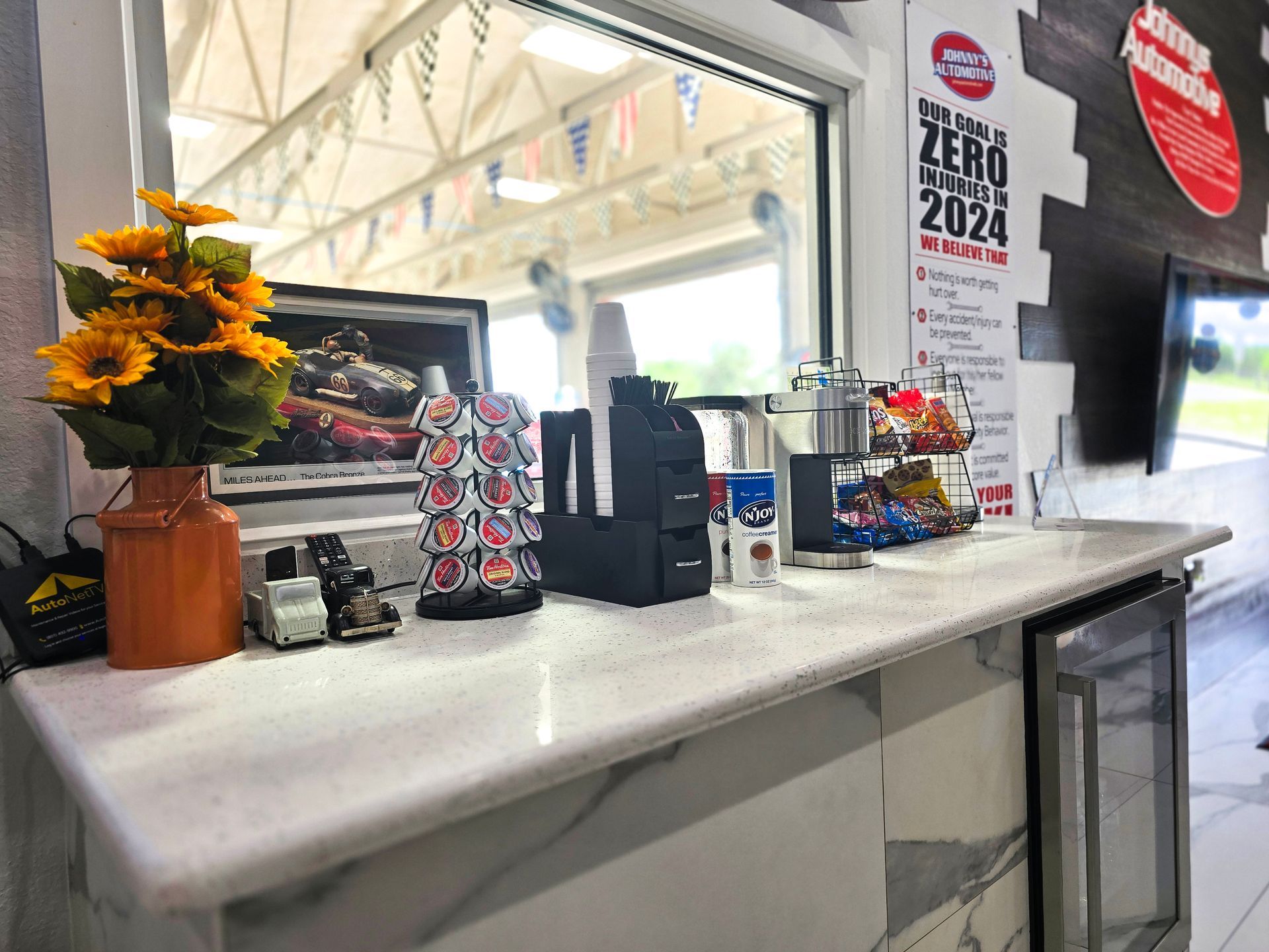 Countertop with snacks and coffee machine at an auto shop, near a window with a view of a parking lot. | Johnny's Automotive