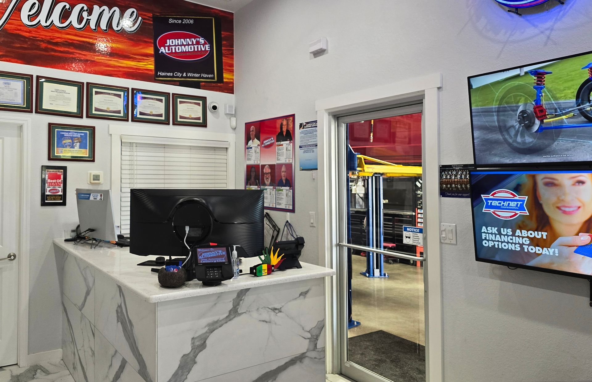 Interior of a car repair shop. Front desk with a computer, diplomas on the wall, and a view into the garage. | Johnny's Automotive