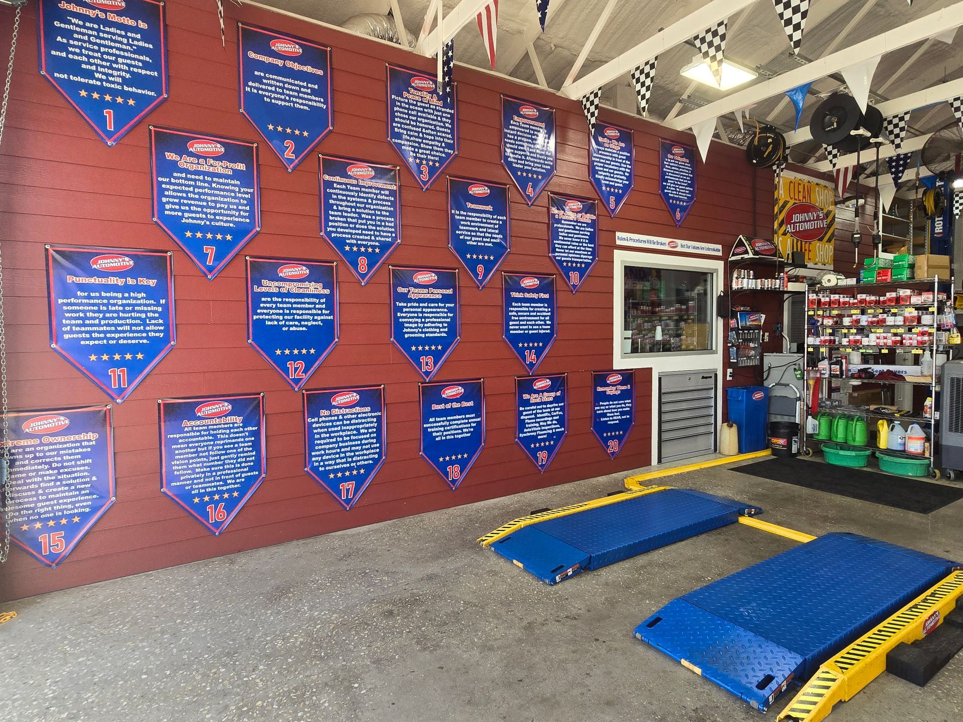 A red-walled auto shop displays awards, with two blue car lifts in front. | Johnny's Automotive
