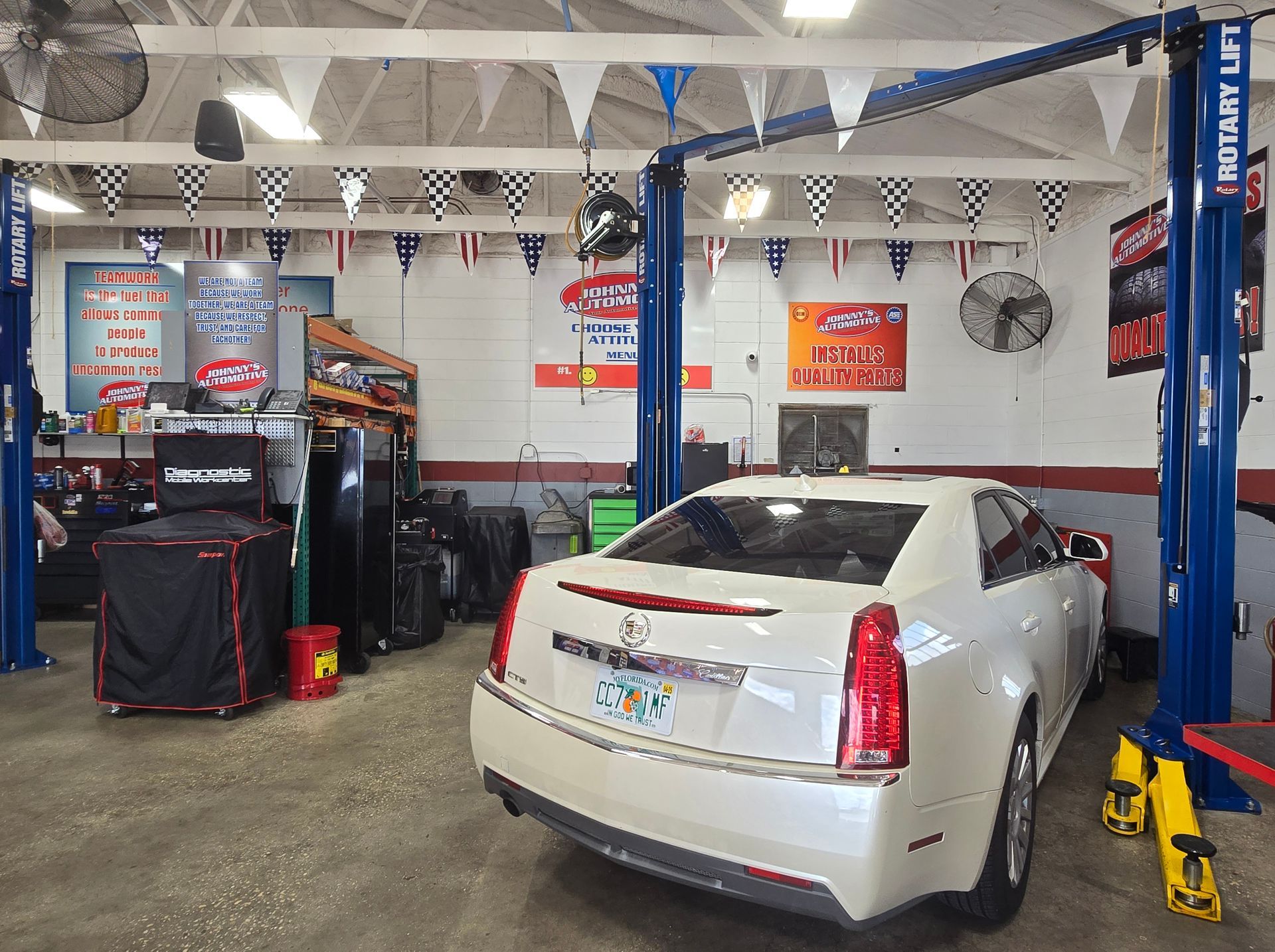 White Cadillac on a lift in a garage, decorated with flags and tools. | Johnny's Automotive