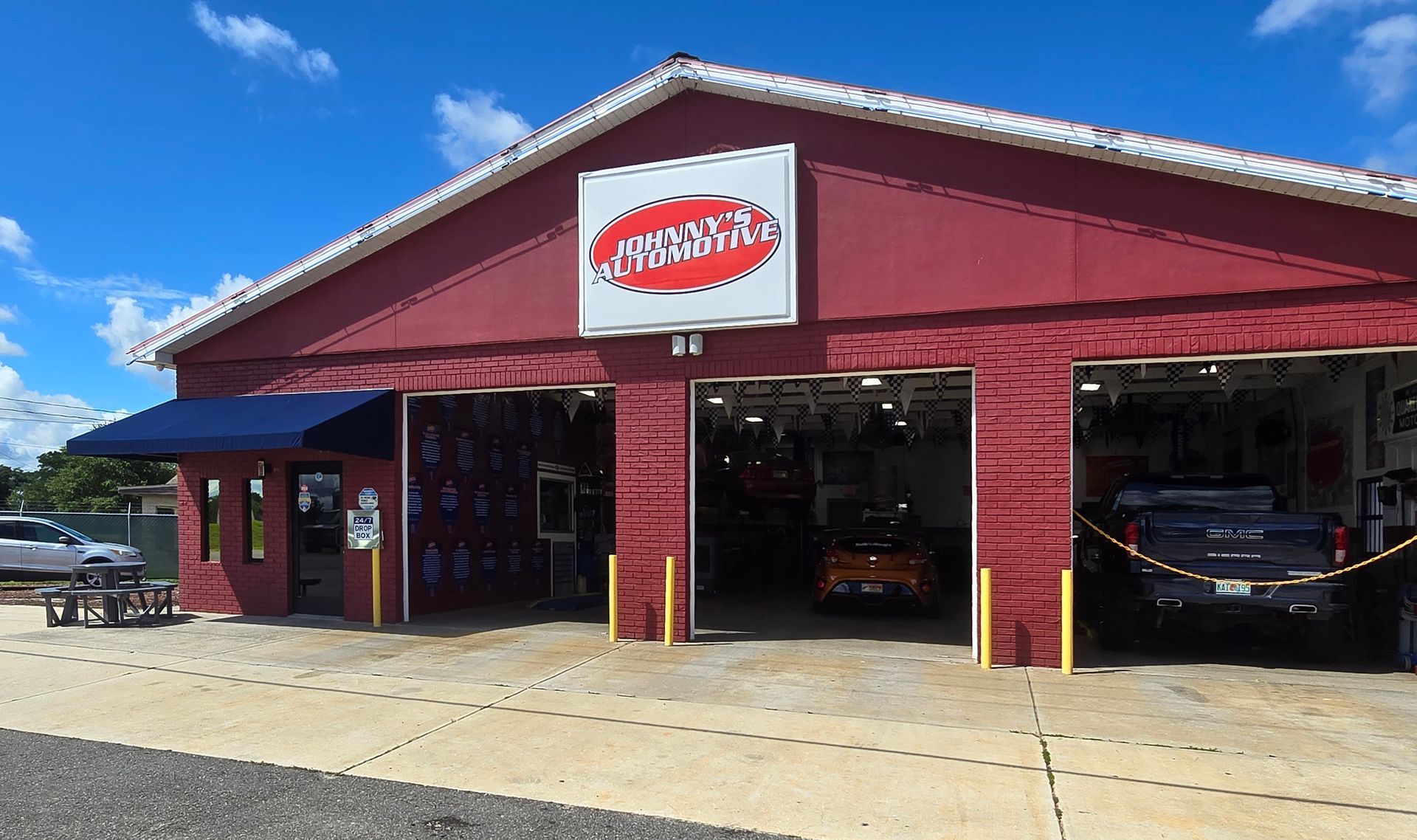 Red auto repair shop with open bays displaying cars under a bright blue sky. | Johnny's Automotive