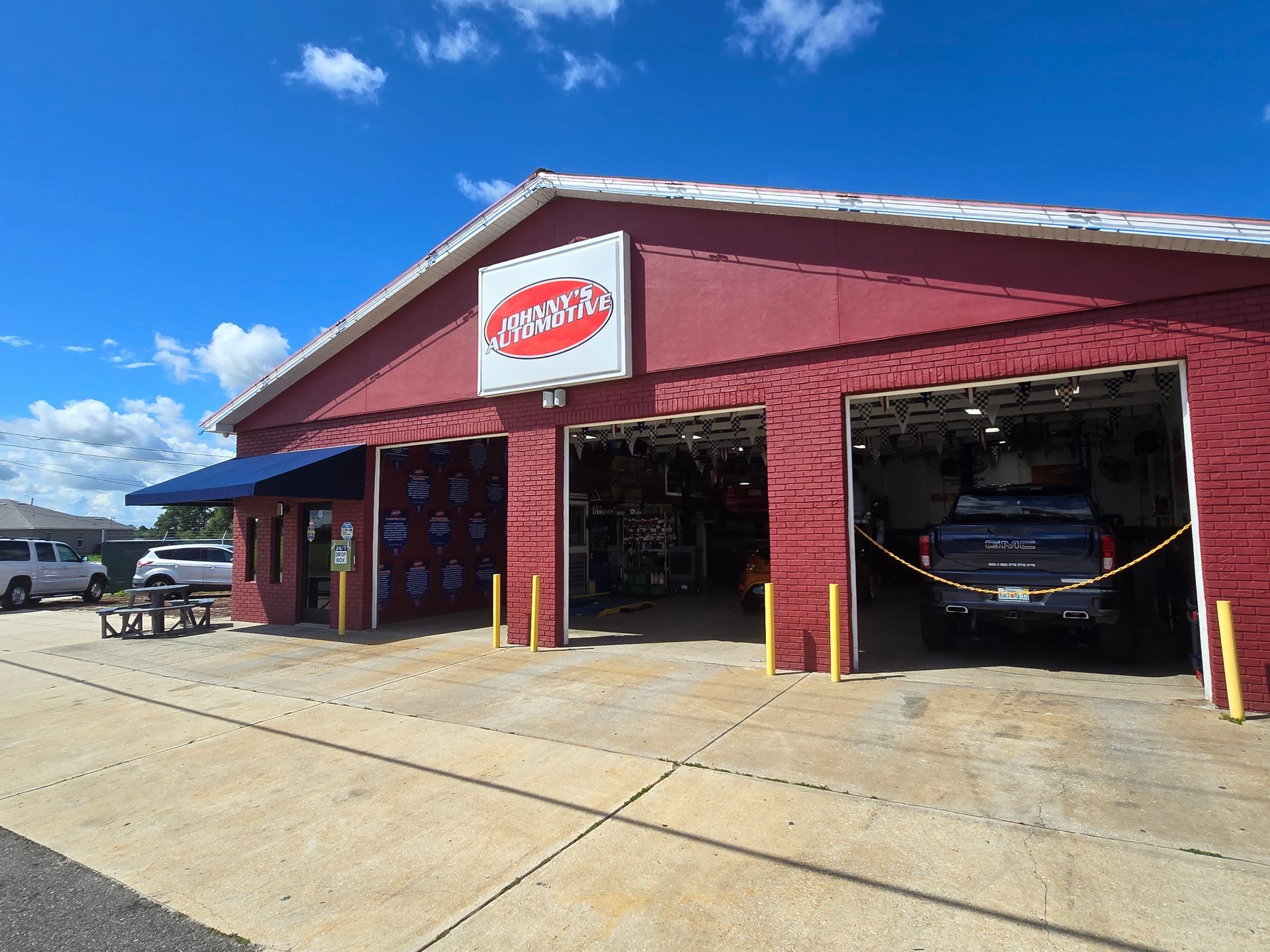 Red auto repair shop with open bays, truck inside, sign above. | Johnny's Automotive