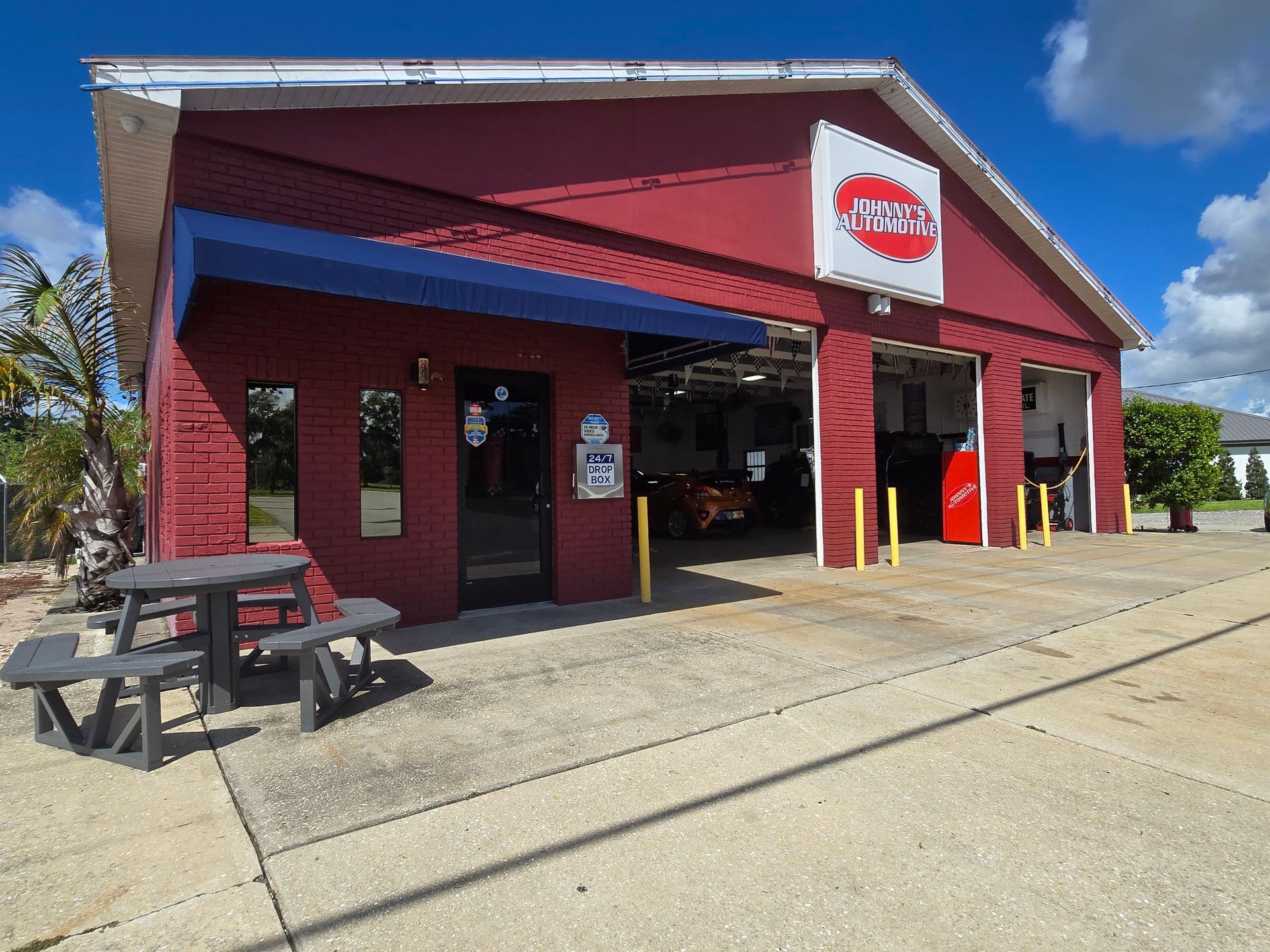 Red auto repair shop with blue awning, open garage bays. Picnic table in front. | Johnny's Automotive