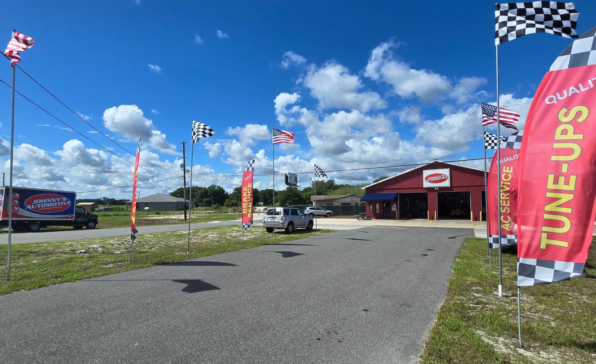 A red auto repair shop with flags on a sunny day; a truck and car are parked outside. | Johnny's Automotive