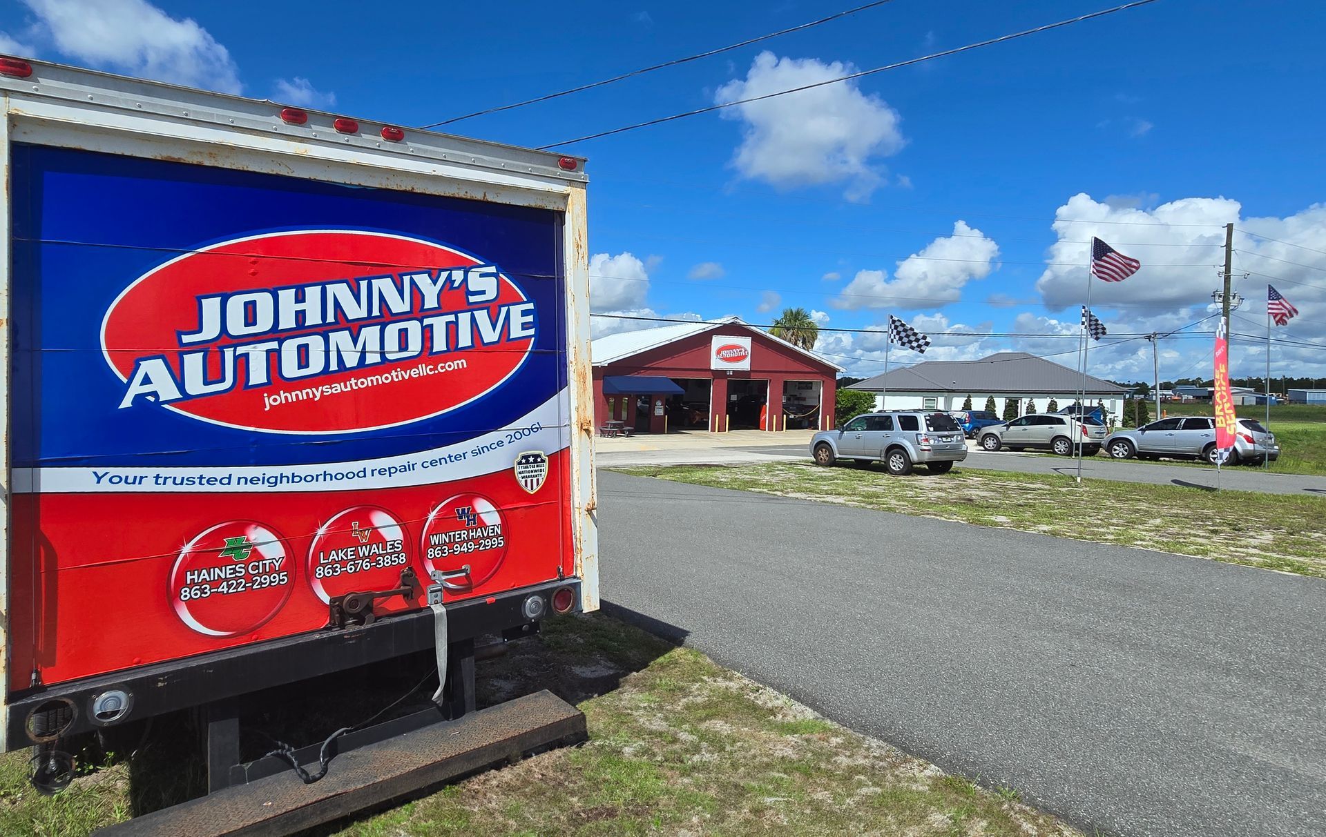 Johnny's Automotive sign on truck, with building and vehicles on a sunny day. | Johnny's Automotive