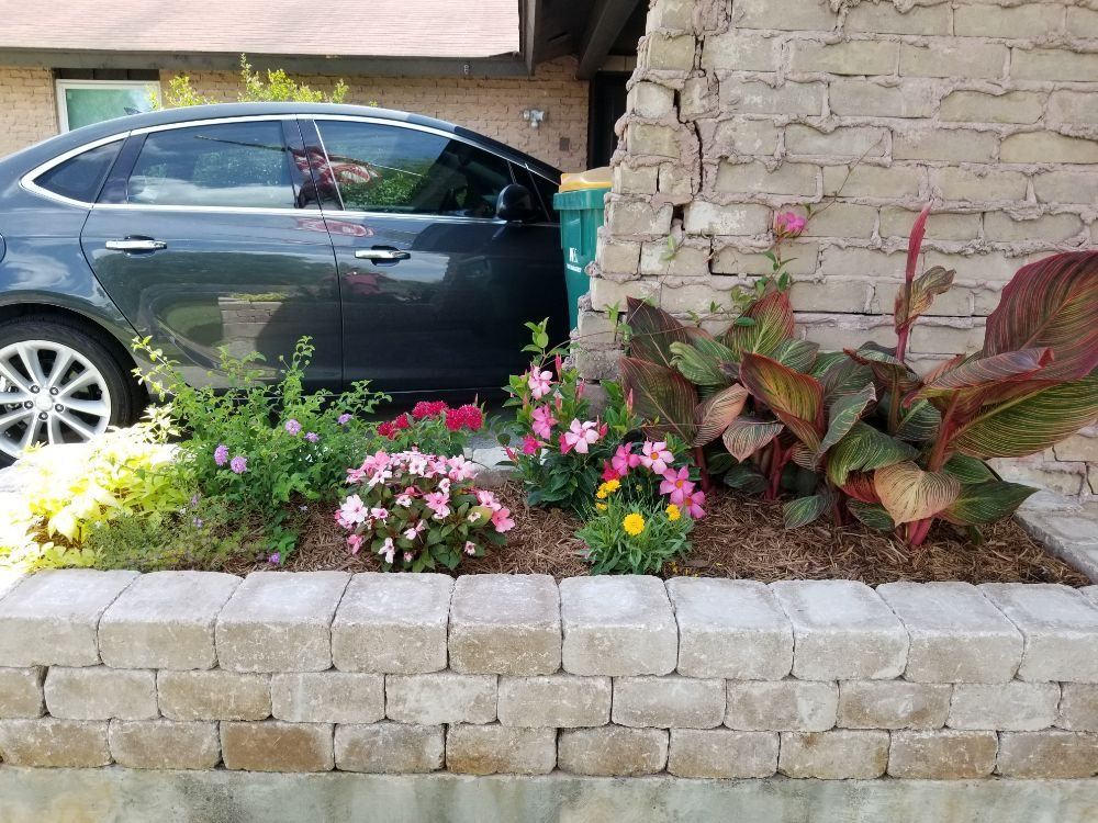 A car is parked in a garden next to a brick wall.