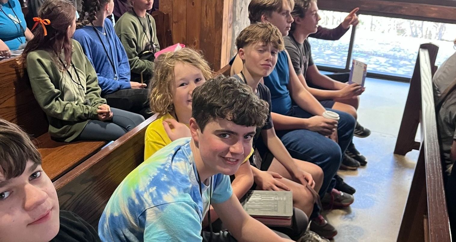 Group of people seated on wooden benches, smiling. Sunlight streams in.
