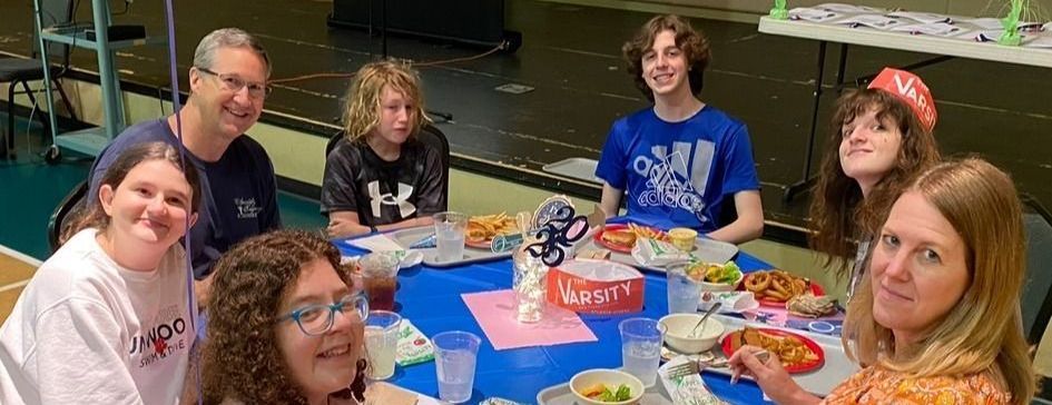 Group of people seated around a blue table with food. They are smiling at the camera.