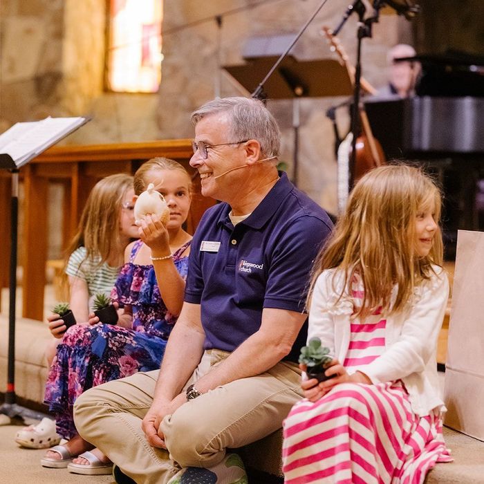 Man smiling, holding shell, with three young girls, small plants, church setting.