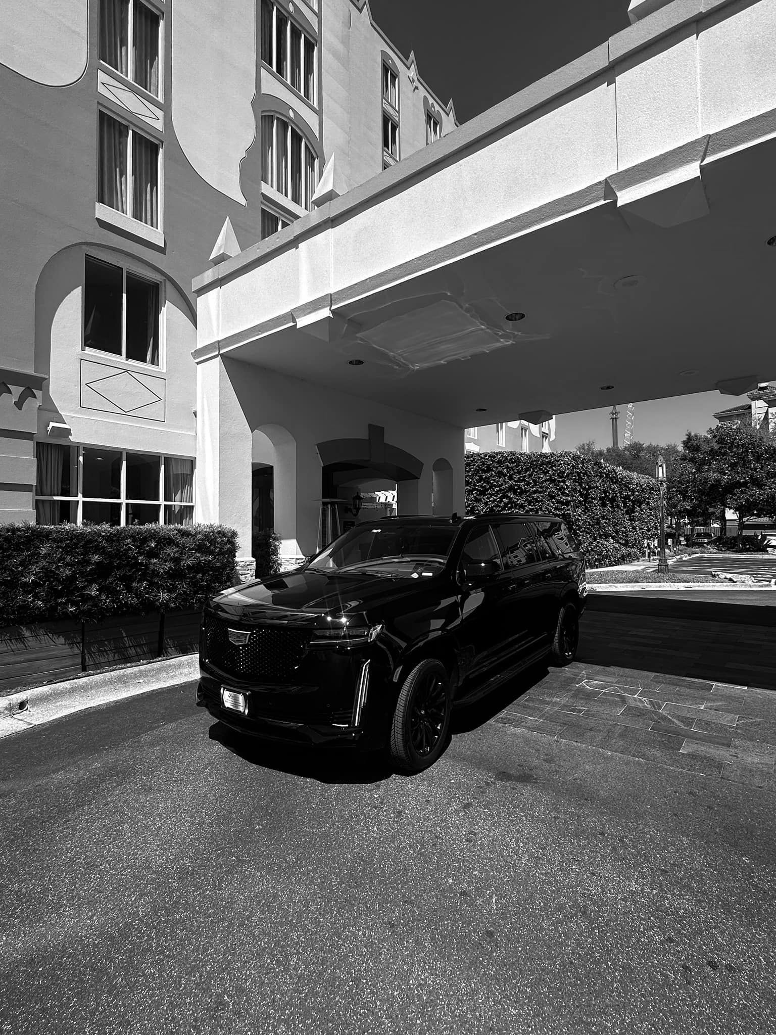 A black and white photo of a car parked under a bridge in front of a building.