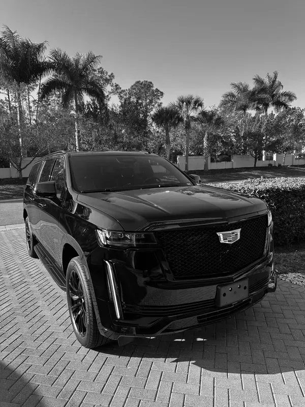 A black and white photo of a cadillac escalade parked on a brick driveway.