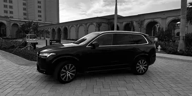 A black and white photo of a volvo xc90 parked in front of a building.