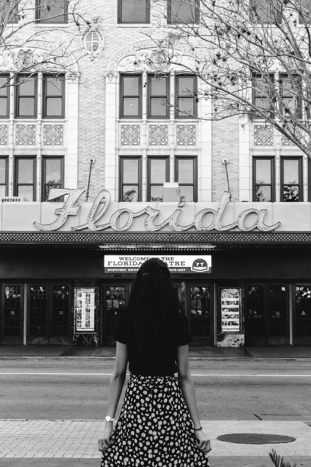 A black and white photo of a woman standing in front of a building.