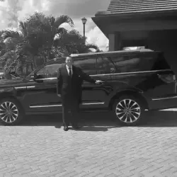 A man in a suit and tie is standing in front of a black suv.