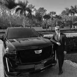 A man in a suit and tie is standing next to a black cadillac.