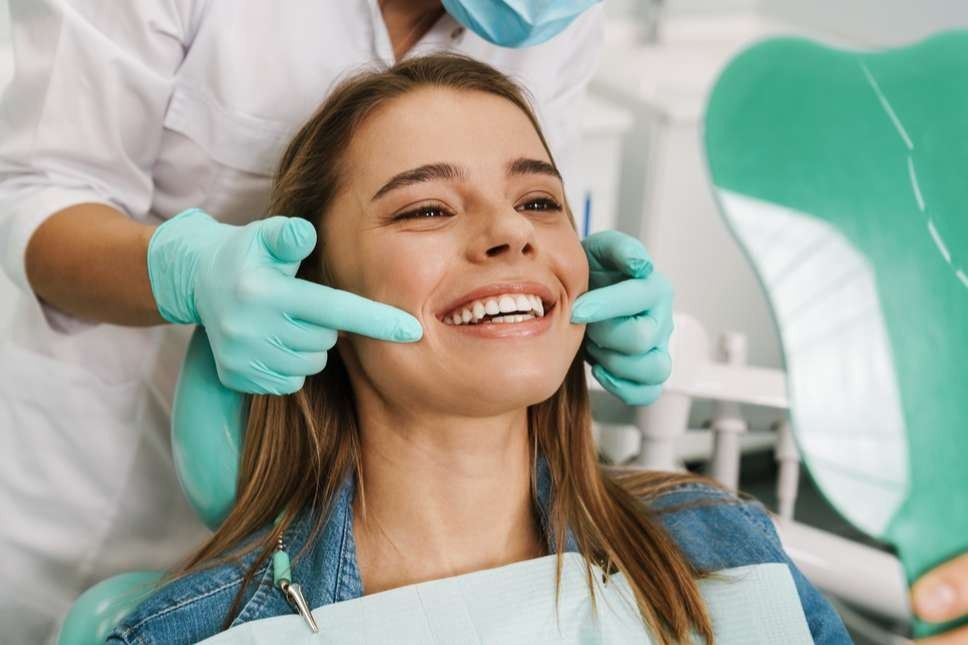 Dentist pointing at patient's teeth, smiling in dental chair.