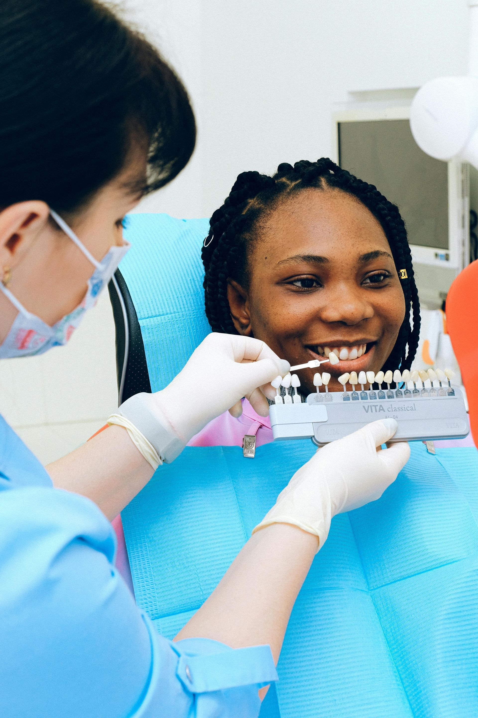 Dentist matching teeth shade with a color guide for a patient in a dental chair.