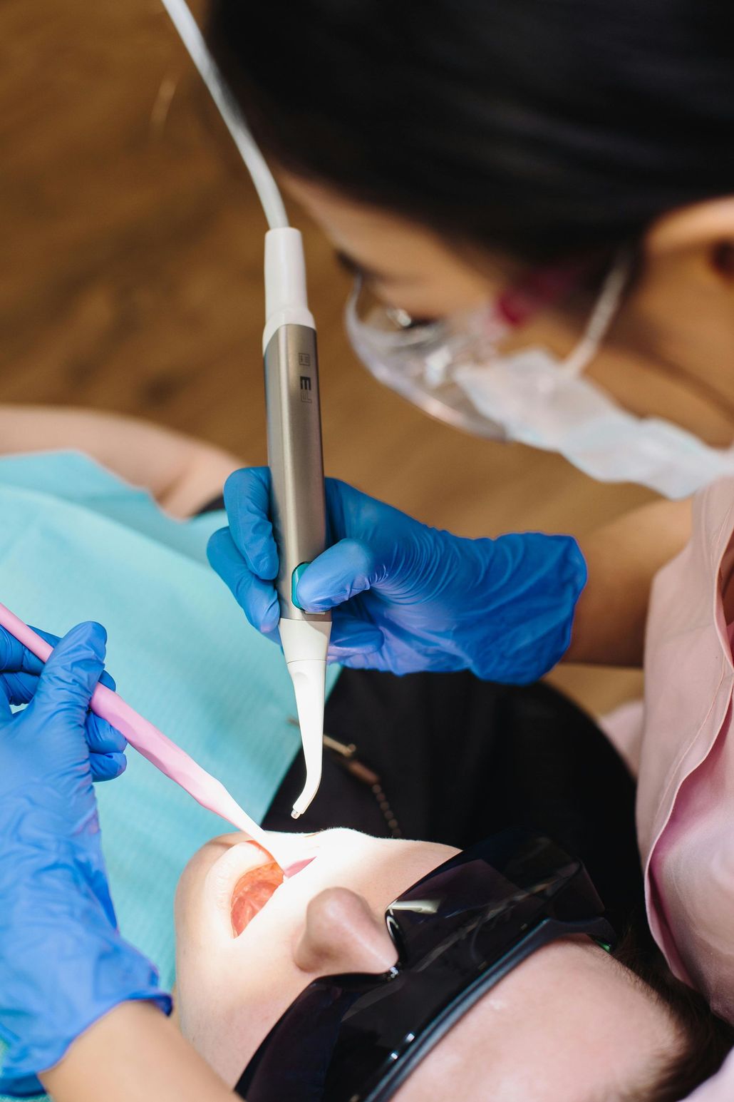 Dentist examining patient's teeth with tools; patient wears eye protection, and dentist wears gloves.