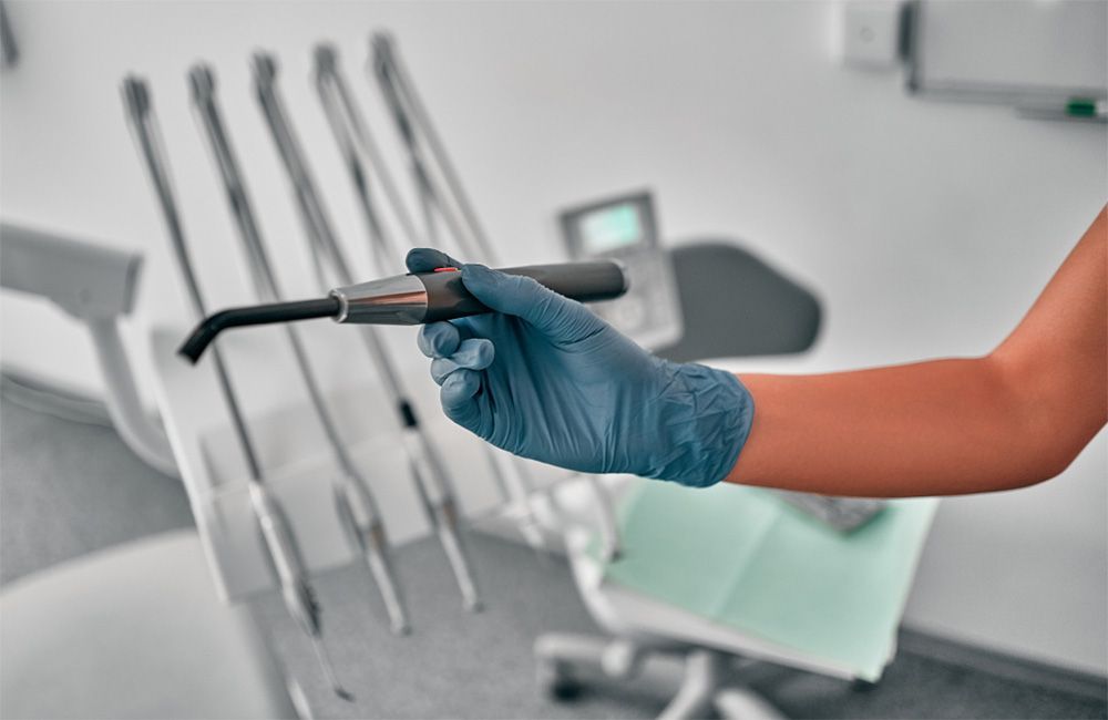 Dentist's gloved hand holding a dental curing light in a clinical setting.