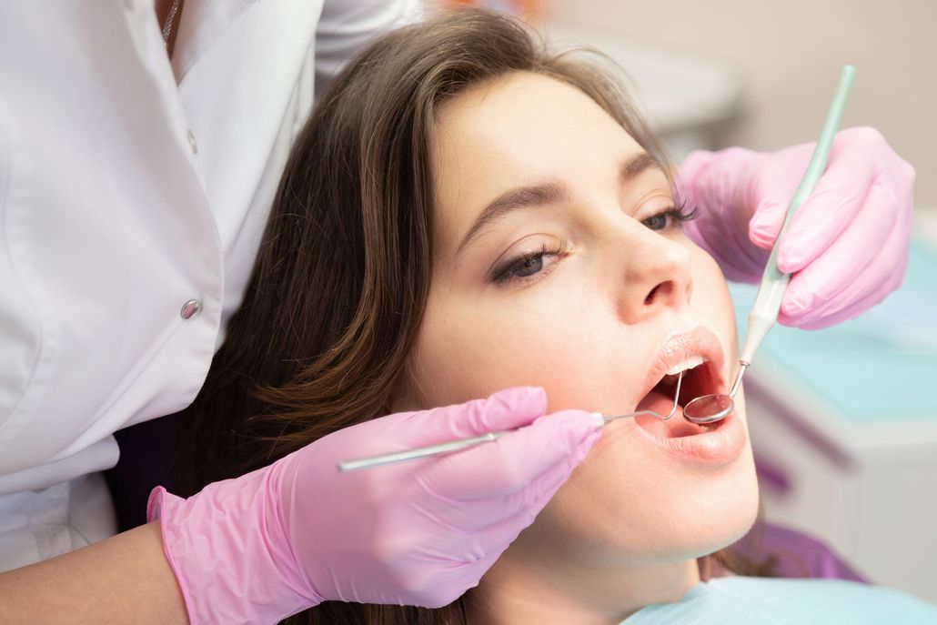 Dentist examining a patient’s open mouth with dental tools and pink gloves