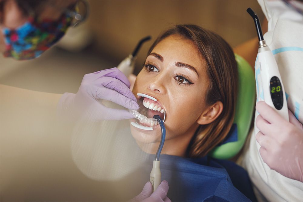 Woman in dental chair, mouth open, receiving dental treatment. Dentist using curing light.
