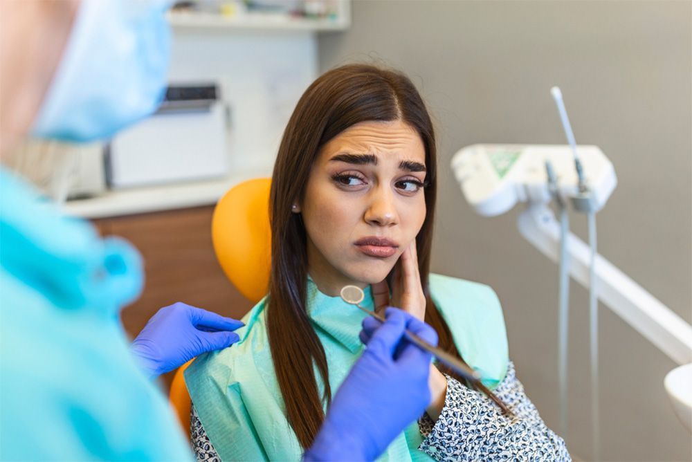 Woman in dental chair, looking pained, with dentist examining her mouth.